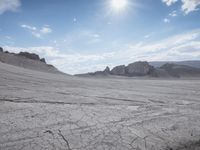 a barren area with many rock and arid terrain in the foreground, some dirt and some water under a bright blue sky