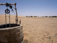 a well is filled with dirt and animals grazing in the background, on a desert plain