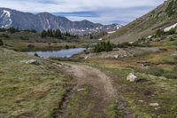 trail leading to mountain peak with clear blue sky above it's ground and green grass, and water running between rocks