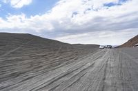 a truck driving on the sand next to a hill covered in sand dune's