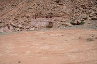 a dirt road through a desert plain with a mountain behind it and a clear blue sky in the background