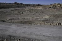 the barren plain is dotted with rocks and dirt in the distance is a dark grey colored hill that has no grass