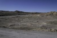 the barren plain is dotted with rocks and dirt in the distance is a dark grey colored hill that has no grass