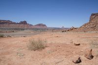 a dirt road through a desert plain with a mountain behind it and a clear blue sky in the background