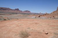 a dirt road through a desert plain with a mountain behind it and a clear blue sky in the background