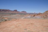 a dirt road through a desert plain with a mountain behind it and a clear blue sky in the background