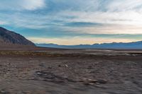 a vehicle is travelling through the dry terrain at sunset time in the desert near mountains