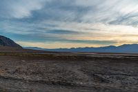 a vehicle is travelling through the dry terrain at sunset time in the desert near mountains