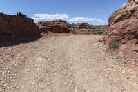 a dirt road with rocks and bushes in the desert on a sunny day and a bright blue sky