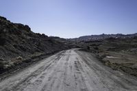 an empty dirt road in the middle of rocks on a sunny day with blue skies