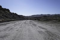 an empty dirt road in the middle of rocks on a sunny day with blue skies