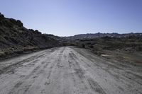 an empty dirt road in the middle of rocks on a sunny day with blue skies