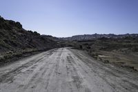 an empty dirt road in the middle of rocks on a sunny day with blue skies