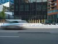 motion blurers as a car passes by a modern building in a city with a large metal screen behind