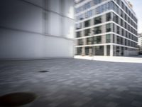 skateboarder performing an trick in a modern city setting with high buildings and cobblestone floor