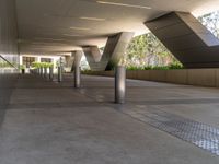 an outside walkway with metal and cement pillars, a bench on one side and a small sidewalk on the other