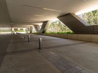 an outside walkway with metal and cement pillars, a bench on one side and a small sidewalk on the other