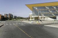 a bus stop at an intersection with a big glass building in the background on the street