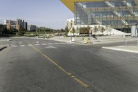 a bus stop at an intersection with a big glass building in the background on the street