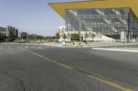 a bus stop at an intersection with a big glass building in the background on the street