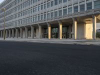 cars driving down a city street near a building with columns in front of it and people walking on the side of the road in front of it