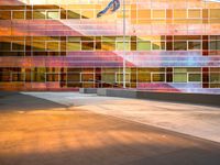 a man on a skateboard in front of a building with colorful glass walls and a flag pole