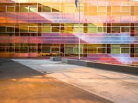 a man on a skateboard in front of a building with colorful glass walls and a flag pole