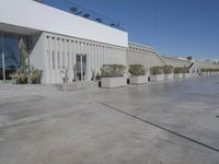 concrete driveway with a parking space for cars and people walking in front of it while a large commercial building with windows and doors sits next to the road