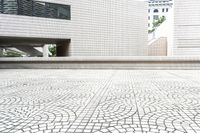 white building with white mosaic pattern in middle of square courtyard with steps leading to other structure