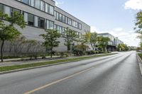 a highway near a building with many windows, and trees lining the side of the road