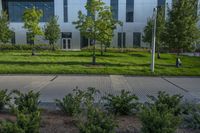 a city street surrounded by grass and tall buildings at the end of a street there is a paved pathway in front of the building