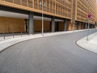 curved road by large office building and sidewalk with no traffic sign on sidewalk beside entrance