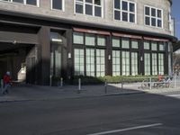 man riding bike past an office building with lots of windows and people walking in the sidewalk