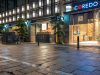 a large brick sidewalk with a store front at night time and a sign that says