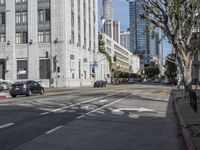 an intersection that is in the middle of the city with cars parked on the street and high rises in the distance