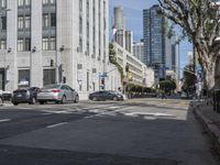 an intersection that is in the middle of the city with cars parked on the street and high rises in the distance