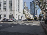 an intersection that is in the middle of the city with cars parked on the street and high rises in the distance