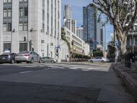 an intersection that is in the middle of the city with cars parked on the street and high rises in the distance