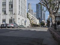 an intersection that is in the middle of the city with cars parked on the street and high rises in the distance