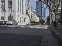 an intersection that is in the middle of the city with cars parked on the street and high rises in the distance