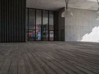 a big wooden floor next to a building with some glass windows and lighting fixtures hanging