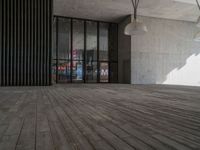 a big wooden floor next to a building with some glass windows and lighting fixtures hanging