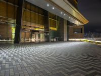 the outside of an office building at night with city lights on it, including a clock, windows and street lights