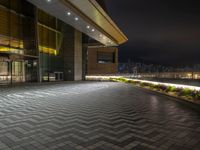 the outside of an office building at night with city lights on it, including a clock, windows and street lights