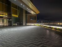 the outside of an office building at night with city lights on it, including a clock, windows and street lights