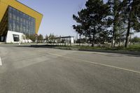 empty street with yellow building and trees in the background behind it - some people crossing the road