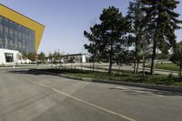 empty street with yellow building and trees in the background behind it - some people crossing the road