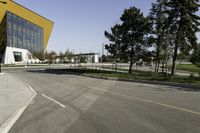 empty street with yellow building and trees in the background behind it - some people crossing the road