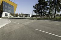 empty street with yellow building and trees in the background behind it - some people crossing the road