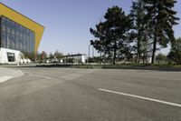 empty street with yellow building and trees in the background behind it - some people crossing the road